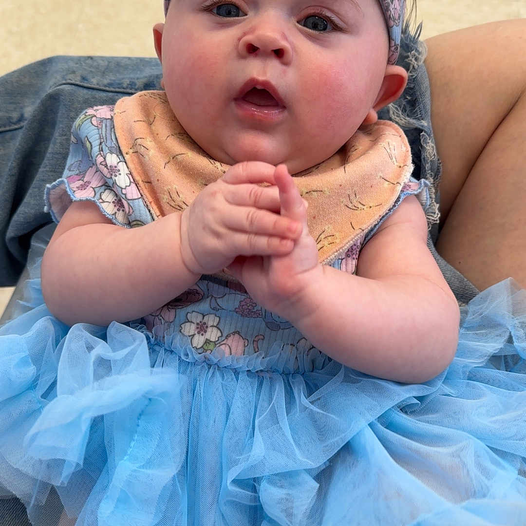 Thalia is registered to the contest to win money with this photo: accessories, baby, bodypart, bonnet, cap, clothing, couch, dress, face, finger, furniture, hand, hat, head, headband, pants, person, photography, portrait, sitting