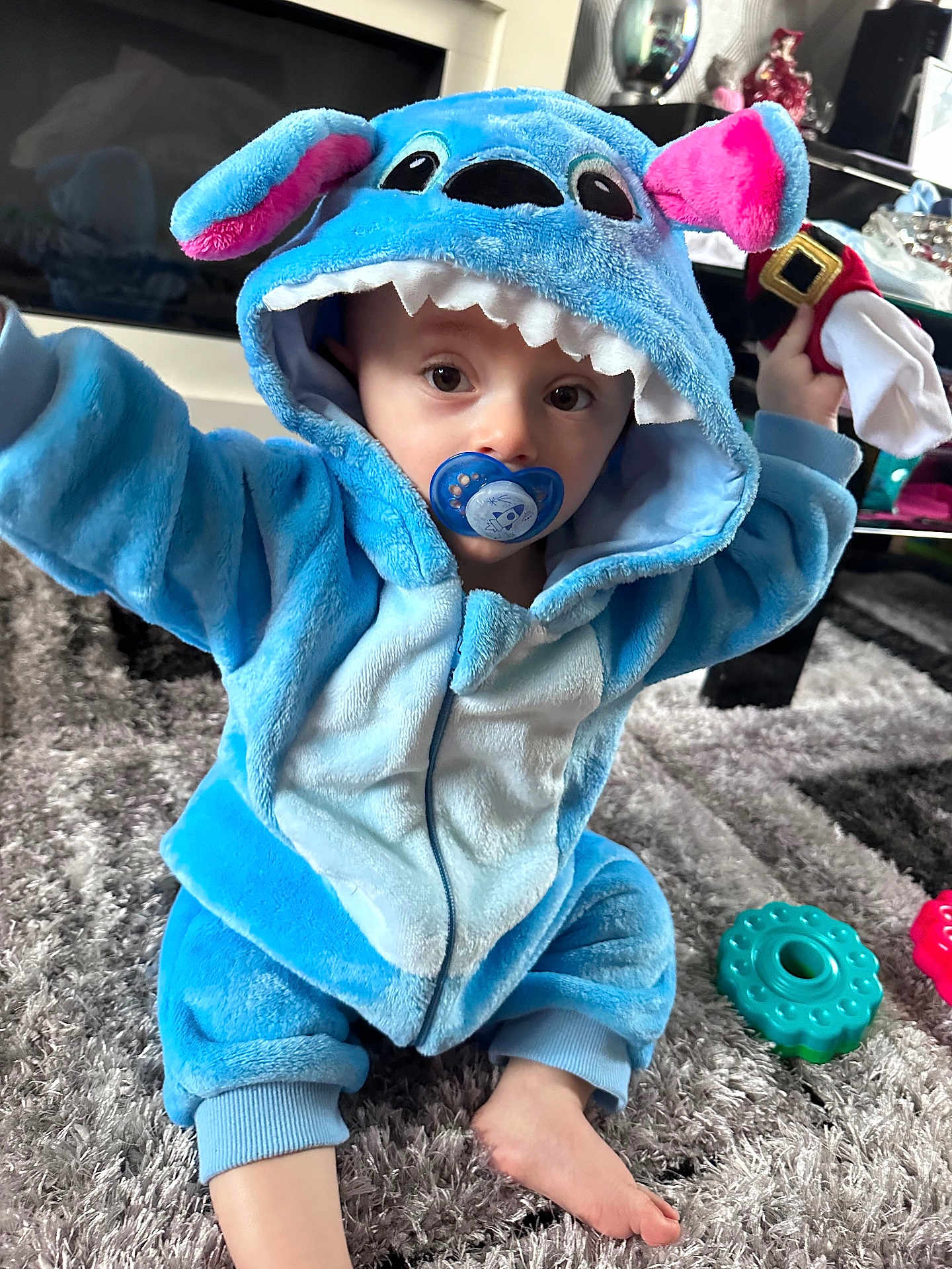 Tommy joined the competition — help win amazing prizes! toddler, child, baby, blue_costume, hoodie, pacifier, toy, carpet, indoor, cute, plush, face, eyes, sitting, foot, hand, play, home, soft, curious