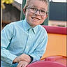 background_blur, boy, casual_clothing, child, daylight, face, fun, glasses, hands, happy, leisure, light_blue_shirt, outdoor, park, person, playground, recreation, short_hair, smile, youth
