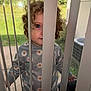 Hollyann joined the competition — help win amazing prizes! child, toddler, curly_hair, vertical_blinds, window, daisy_pattern, sweatshirt, outside, greenery, eye, face, curious, cozy, patterned_clothing, daylight, home, screen_door, hand, portrait, casual