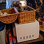 cat, basket, microwave, kitchen, tapestry, bear_face, box, table, window, curtain, food_boxes, storage, indoor, furniture, pet, relaxing, clutter, woven, animal, domestic