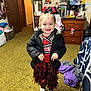 child, girl, cheerleader, pom_poms, black_jacket, white_shoes, carpet, indoor, smile, hair_bow, dresser, books, wall_art, mirror, clothing, toy, room, furniture, happy, person