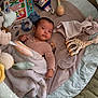 baby, infant, blanket, toy, play_mat, stuffed_animal, giraffe_toy, pacifier, rattle, soft_toy, child, indoors, floor, cute, portrait, lying_down, cozy, colorful, clothing, face