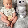 baby, child, plush_toy, koala, blanket, soft_texture, wooden_plaque, sitting, indoors, cute, infant, clothing, portrait, toy, comfortable, young, expression, hands, feet, floor