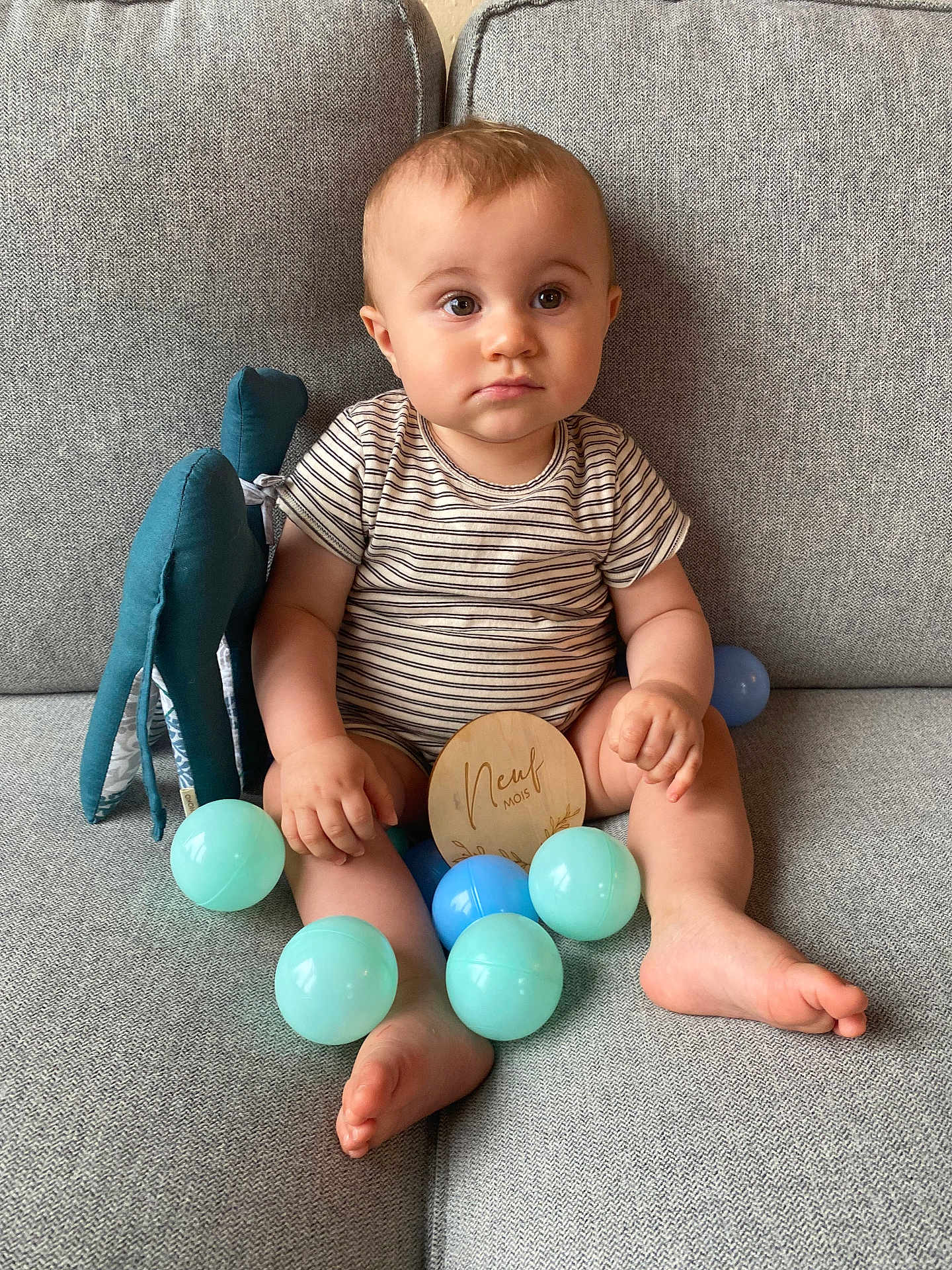 Clovis participe au concours pour gagner de l'argent avec cette photo : baby, child, plush_toy, plastic_balls, couch, striped_clothing, wooden_plaque, sitting, indoors, face, feet, hand, toy, expression, person, furniture, soft_toys, cute, portrait, early_childhood