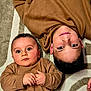 Malone participe au concours pour gagner de l'argent avec cette photo : baby, child, sibling, carpet, brown_clothing, lying_down, indoor, portrait, cute, smile, face, hands, young_child, patterned_carpet, cozy, matching_outfits, curious, eyes, candid, family