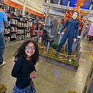 Kimberlee Montero is registered to the contest to win money with this photo: child, girl, smiling, glasses, curly_hair, portrait, halloween, horror, mannequin, mask, costume, retail_store, store_display, seasonal_decor, orange_leaves, haunted_scene, skeleton, indoor, shopping, playful