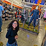 child, girl, smiling, glasses, curly_hair, portrait, halloween, horror, mannequin, mask, costume, retail_store, store_display, seasonal_decor, orange_leaves, haunted_scene, skeleton, indoor, shopping, playful