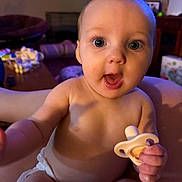 Sutton joined the competition — help win amazing prizes! arm, baby, bare_chest, big_eyes, closeup, cute, diaper, expression, furniture, hand, indoor, infant, living_room, pacifier, portrait, sitting, skin, surprised, toy, wooden_table