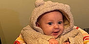 Sutton is registered to the contest to win money with this photo: apparel, baby, child, clothing, curious, cute, expression, face, hands, high_chair, hoodie, indoor, infant, person, seat, smile, table, teddy_bear, wall, young