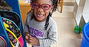 Deshawna joined the competition — help win amazing prizes! backpack, braided_hair, chair, child, classroom, colorful, education, floor, girl, glasses, happy, indoor, jeans, learning, playful, shelf, smiling, sneakers, sweatshirt, toy