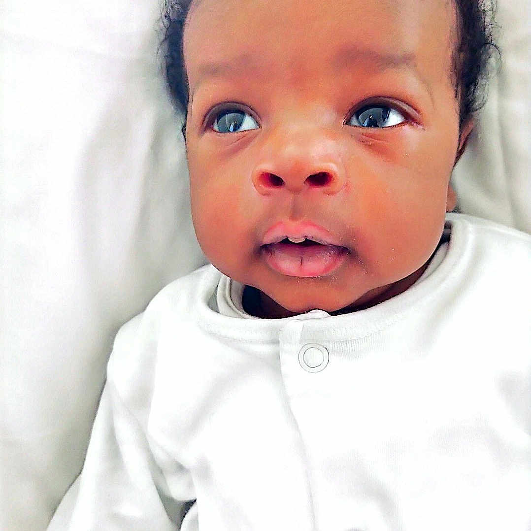 Fope is registered to the contest to win money with this photo: adorable, baby, child, closeup, curly_hair, cute, expression, eyes, face, indoors, infant, lying_down, newborn, peaceful, portrait, skin, sleepwear, soft_light, white_onesie, young