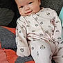 baby, infant, onesie, smiling, face, couch, quilt, patchwork, pink_clothing, cartoon_print, relaxed, indoors, cute, child, young, soft_lighting, seated, comfort, cozy, portrait