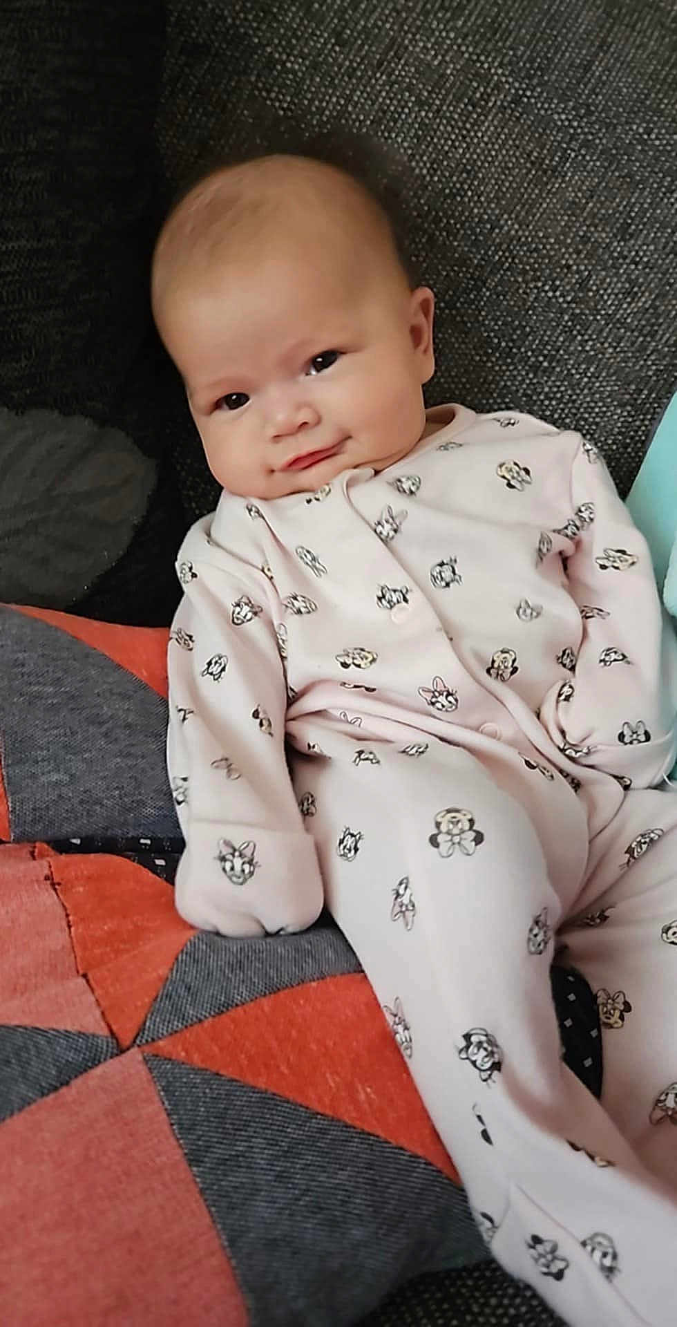Violet joined the competition — help win amazing prizes! baby, infant, onesie, smiling, face, couch, quilt, patchwork, pink_clothing, cartoon_print, relaxed, indoors, cute, child, young, soft_lighting, seated, comfort, cozy, portrait