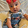 baby, child, red_bow, denim_overalls, patches, curious_eyes, sitting, cushion, soft_background, infant, cute, portrait, closeup, clothing, hand, face, headband, indoor, person, young_child