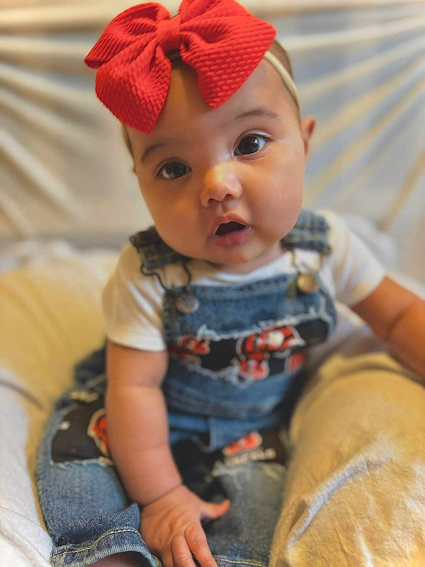 Aurora joined the competition — help win amazing prizes! baby, child, red_bow, denim_overalls, patches, curious_eyes, sitting, cushion, soft_background, infant, cute, portrait, closeup, clothing, hand, face, headband, indoor, person, young_child