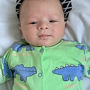 Owen participe au concours pour gagner de l'argent avec cette photo : baby, infant, onesie, green_clothing, crocodile_pattern, blue, face, head, eyes, nose, mouth, skin, lying_down, pillow, white_background, soft_texture, newborn, child, portrait, indoors