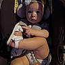 baby, car_seat, headband, flower, sandal, infant, child, footwear, diaper, pacifier, seatbelt, cute, indoors, person, young_child, baby_girl, legs, hand, shadow, sitting