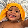 toddler, child, smile, happy, face, teeth, orange_towel, blanket, quilt, skin, bare_chest, earring, closeup, portrait, indoor, cute, baby, expression, joy, relaxation