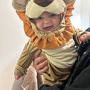 Sacha a rejoint le concours — aidez-le/la à gagner de superbes lots ! baby, infant, child, lion_costume, hood, costume, smile, teeth, eyes, hand, adult_hand, holding, cute, portrait, indoor, towel, black_sleeve, plush, happy, face