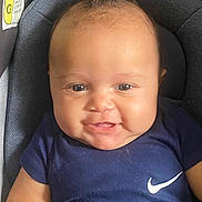 Adonis is registered to the contest to win money with this photo: baby, infant, smiling, face, blue_clothing, nike_logo, car_seat, warning_label, cute, happy, child, portrait, indoor, young, person, head, skin, eyes, mouth, hair