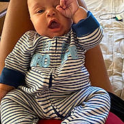 Adonis is registered to the contest to win money with this photo: baby, infant, striped_onesie, person, hand_gesture, indoor, bed, legs, lap, cute, face, expression, child, sleepwear, comfort, relaxed, home, soft_lighting, closeup, seated