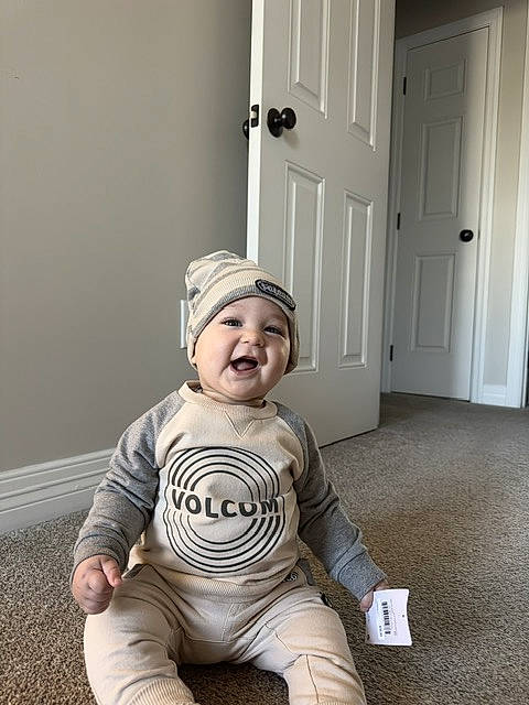 Jamil joined the competition — help win amazing prizes! architecture, baby, babylaughing, cap, clothing, costume, door, face, happy, hat, head, indoors, laughing, pants, person, photography, portrait, sitting, smile, wood