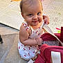 baby, child, smiling, drool, bag, red_bag, play_mat, outdoor, sunlight, white_shoes, concrete_floor, dress, cherry_pattern, curious, cute, person, infant, exploring, sitting, happy
