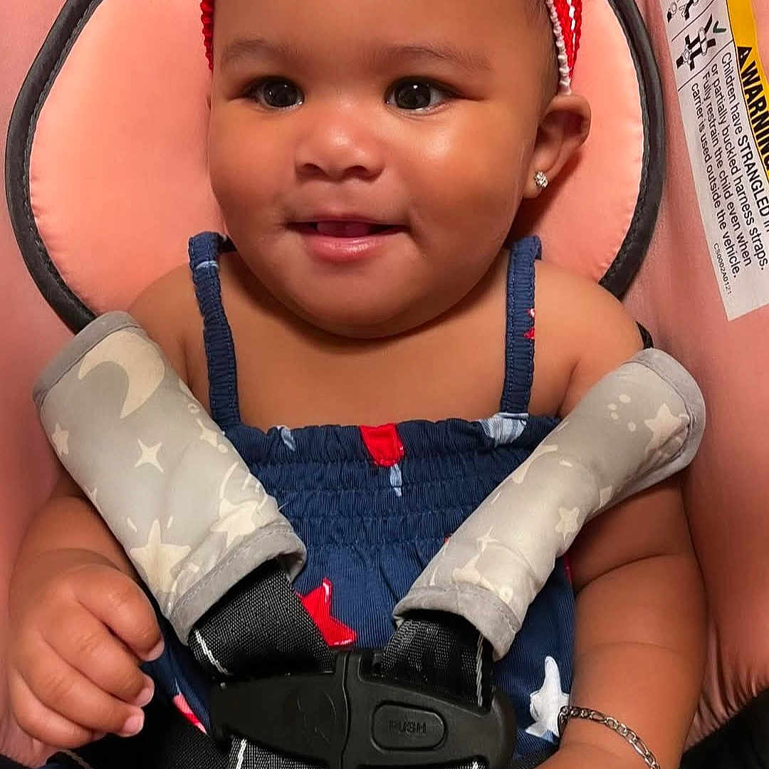 E'Mari is registered to the contest to win money with this photo: arm, baby, bracelet, car_seat, child, clothing, cute, face, hand, happy, headband, indoors, infant, person, safety_buckle, seat, skin, smile, straps, young_child