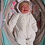 baby, infant, onesie, white_clothing, smiling, bassinet, baby_bed, floral_pattern, headwear, brown_hat, cute, cozy, sleepwear, footed_pajamas, child, happy, indoors, soft_toys, baby_accessories, portrait