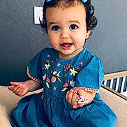 Agata participe au concours pour gagner de l'argent avec cette photo : toddler, child, blue_dress, bows, curly_hair, smile, sitting, indoor, embroidery, hand, face, cute, person, young_child, happy, portrait, clothing, furniture, chair, background