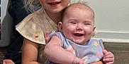 Amelia Stanberry is registered to the contest to win money with this photo: baby, bodypart, clothing, face, furniture, happy, head, indoors, laughing, mouth, newborn, pajamas, pants, person, photography, portrait, shorts, sitting, smile, t_shirt