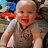 baby, child, infant, smiling, laughing, portrait, indoor, living_room, home, gray_shirt, short_sleeves, seated, close_up, face, eyes, hands, toys, television, furniture, happy