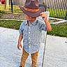 Patrick is registered to the contest to win money with this photo: blue_shoes, boy, brown_pants, casual_clothing, checkered_shirt, child, daylight, fence, footwear, grass, hat, nature, outdoor, park, person, playground, posing, sidewalk, tree, young_child