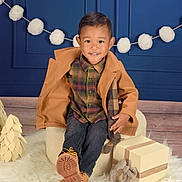 Patrick joined the competition — help win amazing prizes! child, smiling, plaid_shirt, tan_coat, jeans, boots, gift_box, chair, fluffy_rug, pom_pom_garland, blue_wall, holiday_decor, indoor, portrait, cute, happy, fashion, cozy, wood_floor, celebration