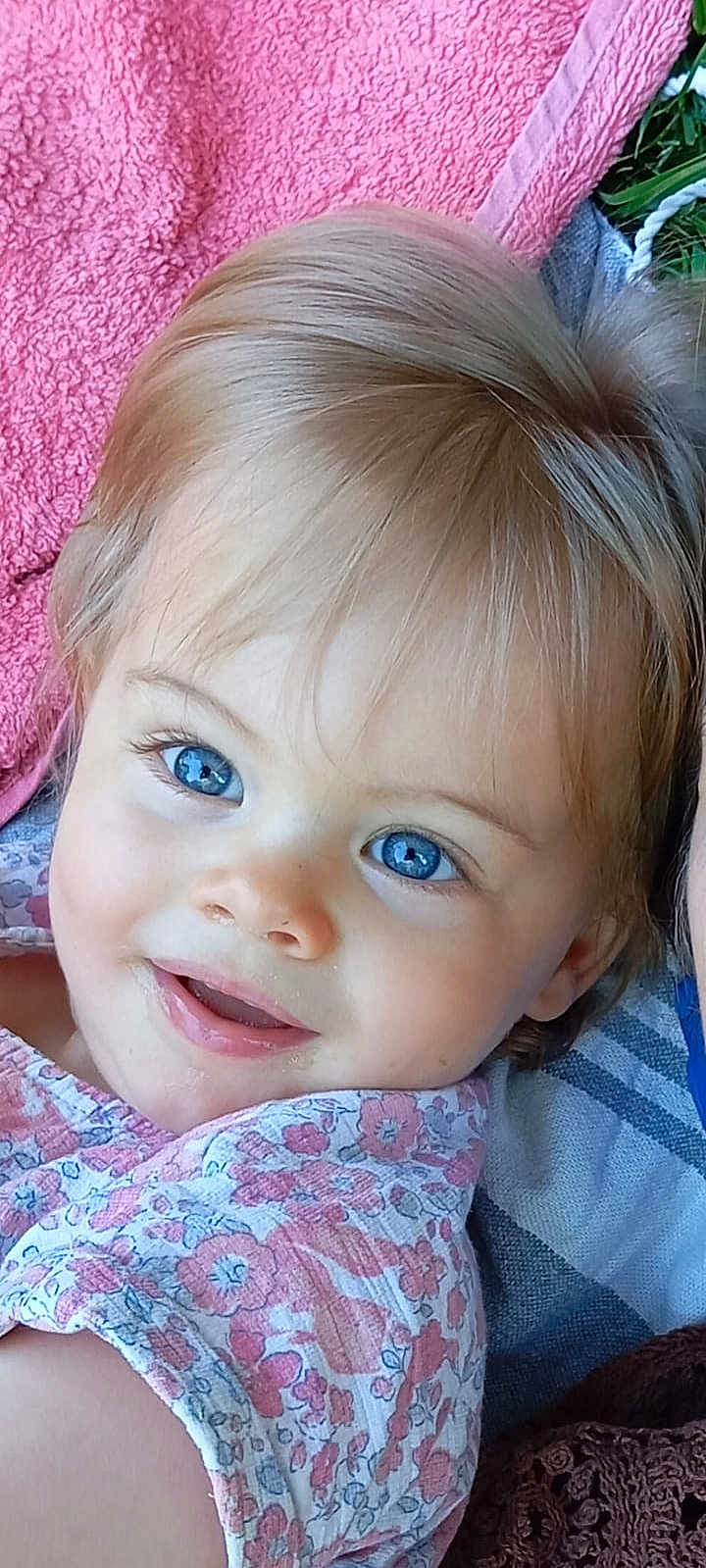 Charlie participe au concours pour gagner de l'argent avec cette photo : toddler, child, smiling, blue_eyes, blond_hair, floral_clothing, face, portrait, close_up, outdoor, towel, grass, happy, skin, eyelashes, baby, person, cute, head, expression