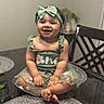 baby, child, smiling, girl, green_dress, headband, bow, sitting, table, dining_room, furniture, indoor, cute, portrait, happy, cross_legged, flower_embroidery, skin, toes, person
