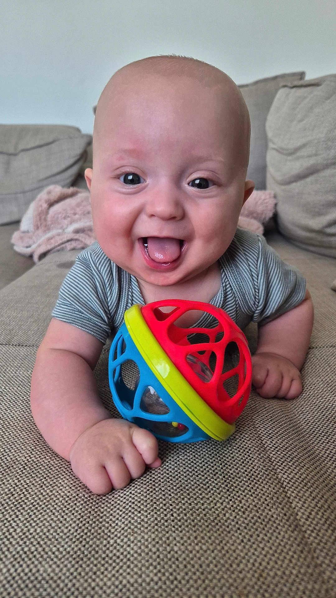 Louis participe au concours pour gagner de l'argent avec cette photo : baby, smiling, tongue_out, toy, colorful, couch, blanket, infant, happy, face, hand, clothing, indoors, child, person, playful, closeup, cute, expression, home