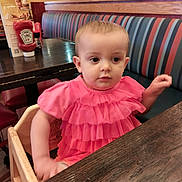 Remi joined the competition — help win amazing prizes! toddler, child, high_chair, pink_dress, restaurant, table, wooden_furniture, booth_seating, striped_cushion, indoor, curious, portrait, baby, dining, neon_sign, television, food_menu, ketchup_bottle, casual_clothing, cute