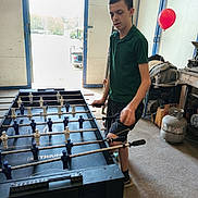 Mikha joined the competition — help win amazing prizes! activity, black_shorts, casual, chair, concrete_floor, daylight, foosball_table, game, garage, green_shirt, hobby, indoor, leisure, metal_gas_tank, open_door, playing, red_balloon, sports, teenage_boy, young_person