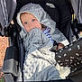 baby, blanket, stroller, child, blue_eyes, hooded_blanket, outdoor, sunlight, person, infant, seat, comfort, soft_texture, nibble, black_stroller, patterned_handle, face, curious, wrapped, clothing