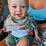 Caiden is registered to the contest to win money with this photo: baby, child, smile, blue_eyes, bib, pacifier, woman, lap, green_clothing, tank_top, indoor, happy, people, family, holding, close_up, skin, hand, face, sitting