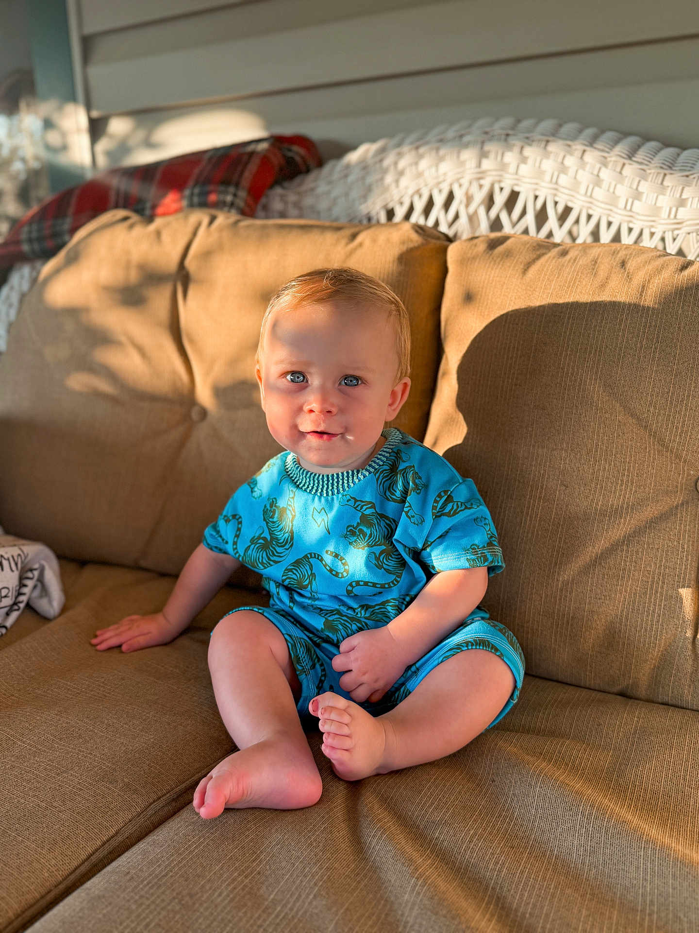 Caiden is registered to the contest to win money with this photo: barefoot, beige, blue_outfit, child, couch, cozy, cute, expression, home, indoor, plaid_blanket, portrait, shadow, sitting, smile, sunlight, tiger_print, toddler, wicker_furniture, young_child