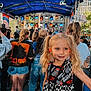 child, girl, concert, crowd, stage, outdoor, earplugs, blonde_hair, pigtails, dress, checkered_pattern, vans, festival, lights, blue_canopy, people, urban, daytime, smile, music