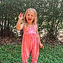 child, girl, smiling, outdoor, greenery, grass, plants, summer, happy, playful, peace_sign, jumpsuit, pink, orange, footwear, sandals, long_hair, nature, sunlight, expression