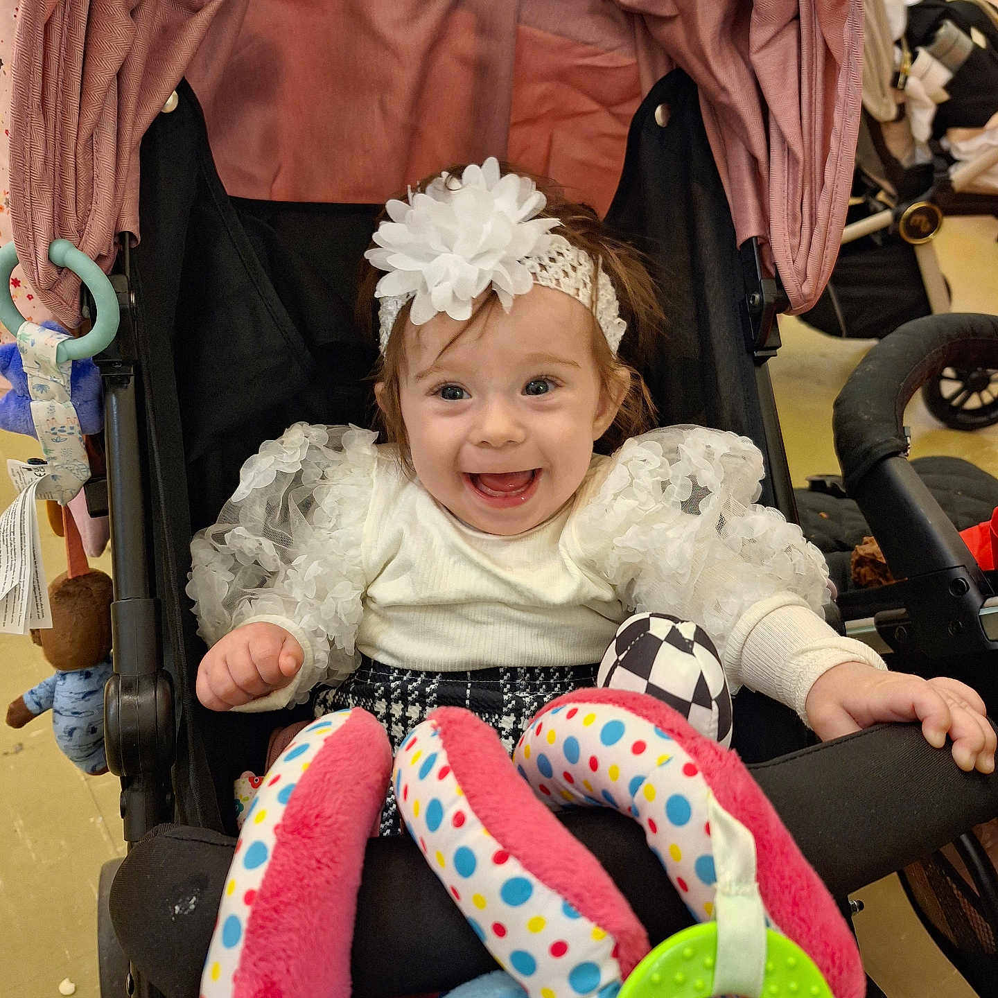 Illianna is registered to the contest to win money with this photo: accessory, baby, child, clothing, colorful, cute, fabric, face, hand, happy, headband, indoor, infant, patterned, person, playful, seat, smiling, stroller, toy