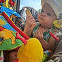 baby, child, hat, sunhat, necklace, biscuit, toy, plush_toy, colorful, seat, car_seat, outdoor, daylight, face, hand, clothing, summer, expression, person, closeup