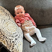 Mckinley is registered to the contest to win money with this photo: baby, child, girl, smile, couch, pillow, headband, cardigan, dress, tights, indoor, cute, infant, happy, portrait, fabric, texture, relaxing, seated, home