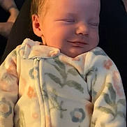 Harley is registered to the contest to win money with this photo: baby, sleeping, onesie, floral_pattern, infant, peaceful, smile, closeup, hands, soft_lighting, indoors, comfort, child, person, young, cute, resting, newborn, cozy, portrait