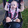 toddler, child, stroller, outdoor, grass, sidewalk, pink_shoes, heart_pattern, raised_arms, happy, messy_face, clothing, seatbelt, black_tray, leaves, daylight, person, cute, playful, nature